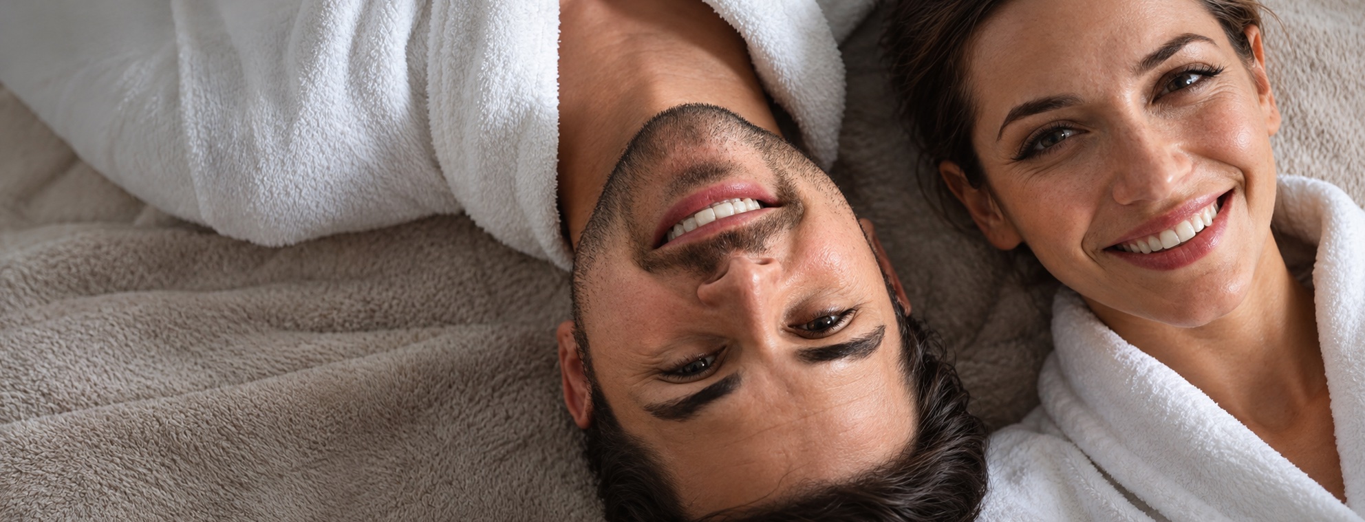 Smiling couple in white spa robes lying head to head